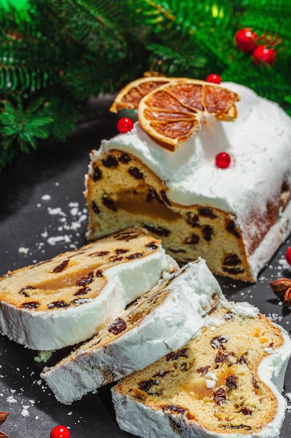 Traditional Christmas stollen German cake European pastry fragrant home baked bread with spices and dried fruit Xmas tree branches and decorations black background close up