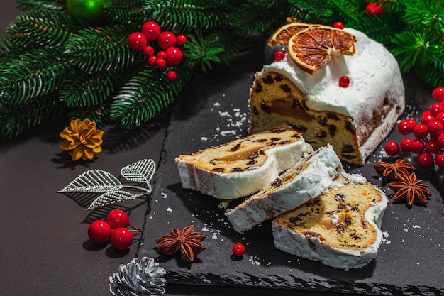 Traditional Christmas stollen German cake European pastry fragrant home baked bread with spices and dried fruit Xmas tree branches and decorations black background copy space