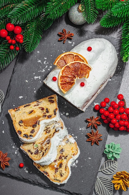Traditional Christmas stollen German cake European pastry fragrant home baked bread with spices and dried fruit Xmas tree branches and decorations black background top view