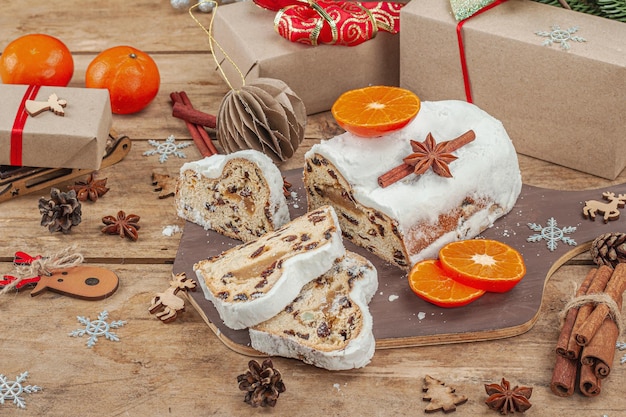 Traditional Christmas stollen German cake European pastry fragrant home baked bread with spices and dried fruit Xmas tree branches and decorations wooden background close up