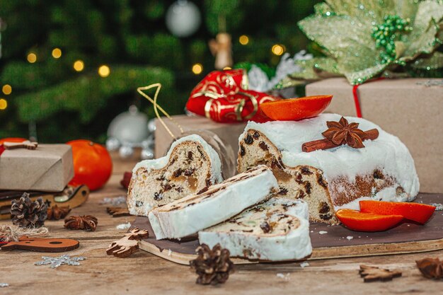 Traditional Christmas stollen German cake European pastry fragrant home baked bread with spices and dried fruit Xmas tree branches and decorations wooden background close up