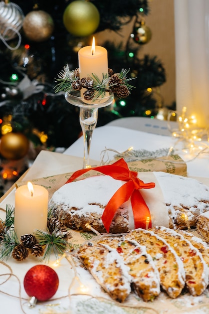 Traditional Christmas stollen made of dried fruits and nuts sprinkled with powdered sugar on the background of a Christmas decor with candles. Traditional Christmas cupcake.