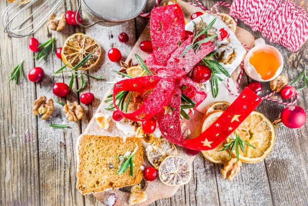 Traditional Christmas and winter holidays baking. Fruit cake with icing, nuts, berry dry orange and rosemary. Sweet homebaked cake on old wooden background with Christmas decoration