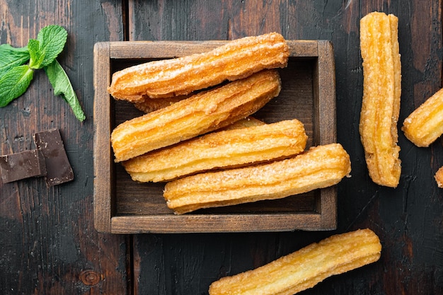 Traditional churros sticks with cinnamon and sugar powder on old dark wooden table background top view flat lay