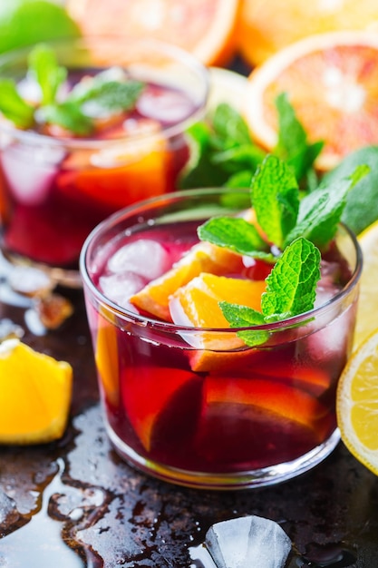 Traditional cold spanish sangria cocktail with red wine and ingredients on a black table citrus fruit orange lime lemon mint leaves and ice for hot summer days