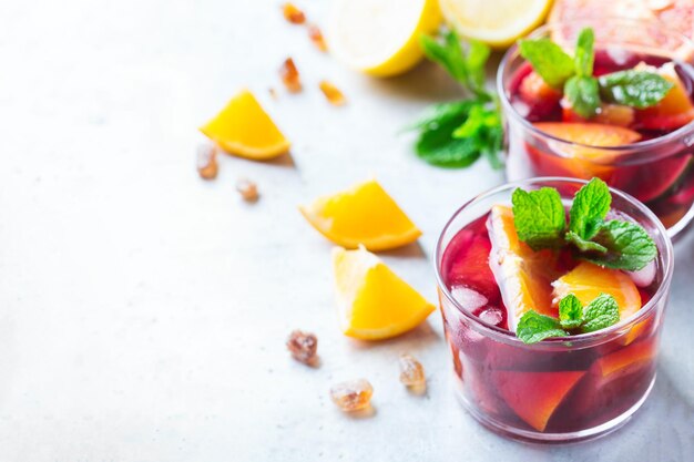 Traditional cold spanish sangria cocktail with red wine and ingredients on a white table citrus fruit orange lime lemon mint leaves and ice for hot summer days copy space background