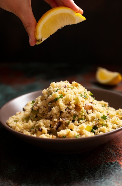 Traditional couscous with vegetables and herbs in a bowl. Lemon in hand. Levantine vegetarian salad. Lebanese, arabic cuisine. Close-up