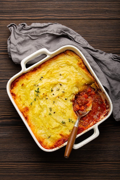 Traditional dish of British cuisine Shepherd's pie casserole with minced meat and mashed potatoes in ceramic baking dish on white rustic table with spoon from above