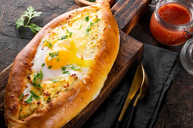 Un piatto tradizionale della cucina georgiana adjarian khachapuri con formaggio e uova e pomodoro piccante