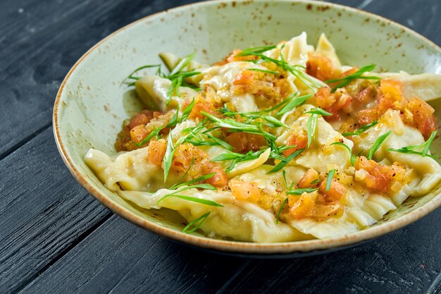 Traditional dish of Israeli cuisine - chicken kreplach with tomato salsa and green onions in a plate on a black wooden surface. Restaurant food. Dumplings with different fillings