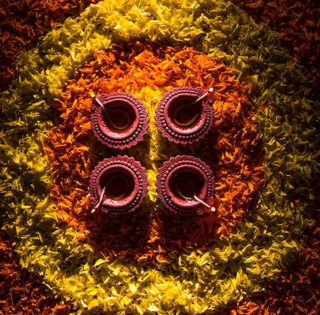 Foto diya tradizionale o lampada a olio accesa su rangoli colorati costituiti da petali di fiori, durante il festival delle luci chiamato diwali o deepawali, messa a fuoco selettiva