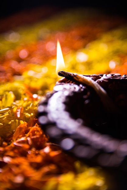 Фото Традиционная дия или масляная лампа, освещенная на красочных ранголи, составленных из цветочных лепестков, на фестивале огней, называемом дивали или дипавали, выборочный фокус
