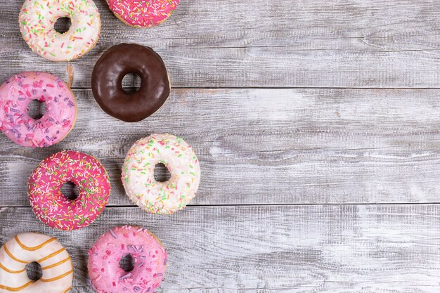 Traditional doughnuts with multicolored glaze laid out on white painted wooden table. Top view, copy space.