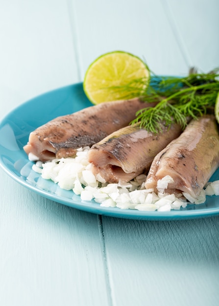 Traditional dutch food freshly salted herring fish with onion called hollandse nieuwe on turquoise plate and wooden surface. European food concept with copy space