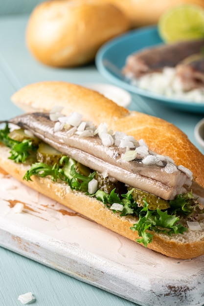 Traditional dutch snack, seafood sandwich with herring, onions and pickled cucumber. Broodje haring. Close up