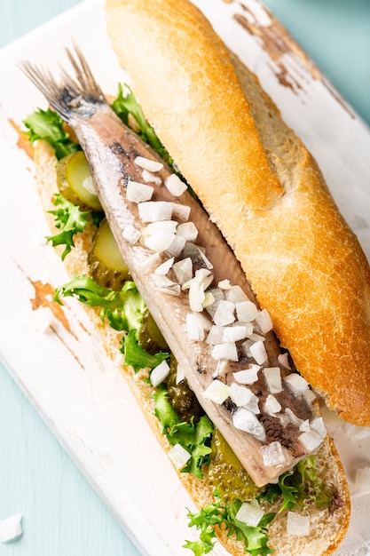 Traditional dutch snack, seafood sandwich with herring, onions and pickled cucumber. Broodje haring