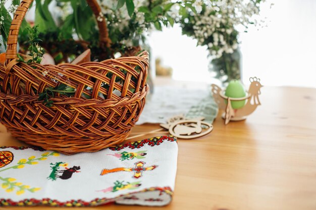 Традиционная пасхальная корзина с едой для благословения в церкви и традиционное украинское вышитое полотенце для покрытия корзины на деревянном столе со свечой и зелеными ветвями самшита и цветами