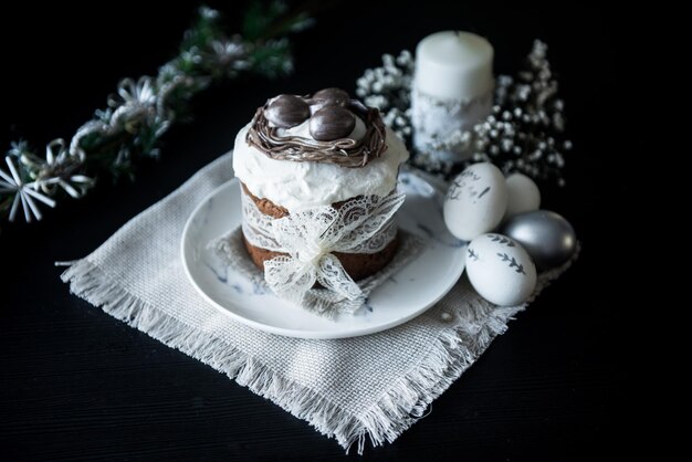 Traditional Easter cake with silver painted eggs candles and willow on a black background Selective focus