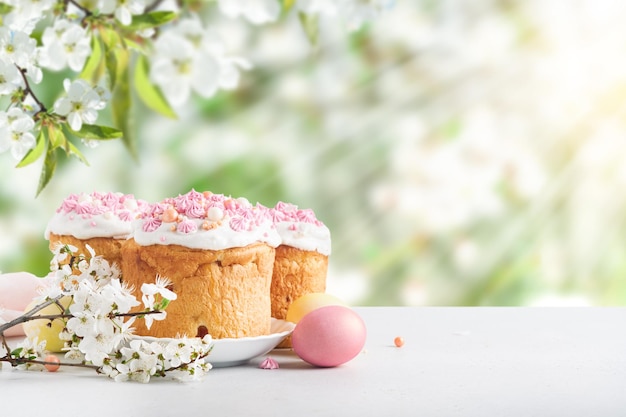 Фото Традиционный пасхальный торт с белым швейцарским меренгом и розовым сладким украшением и красочными окрашенными яйцами на фоне цветущей вишни или яблочного сада, затопленного солнечным светом и лучами с копировальным пространством
