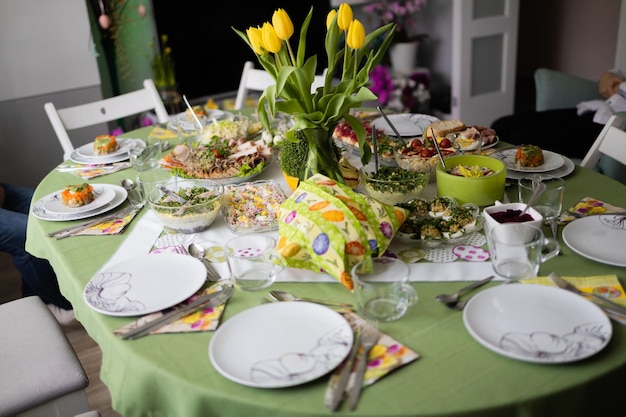 Traditional Easter dishes with white borscht sausage eggs salad and cakes on festive table in Poland Home interior with easter decor Spring flowers in a vases easter eggs on a light background