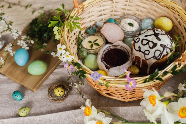 Traditional Easter food in basket Homemade easter bread natural dyed easter eggs ham beets butter cheese on rustic table with spring blossoms and linen napkin Top view