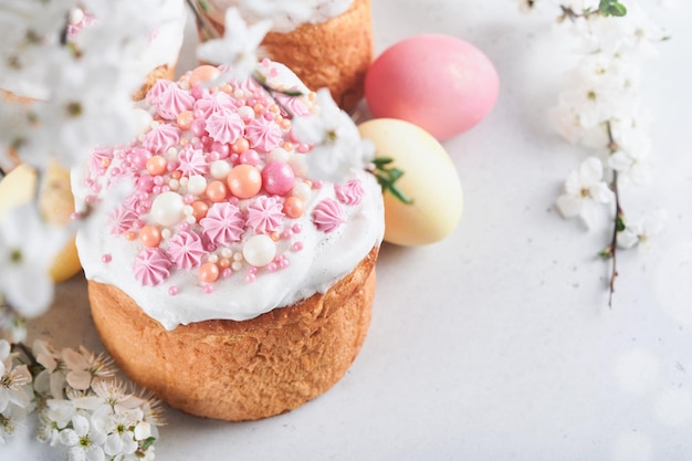 Traditional Easter sweet bread or cakes with white icing and sugar decor colored eggs and cherry blossom tree branch over white table Various Spring Easter cakes Happy Easter day Selective focus