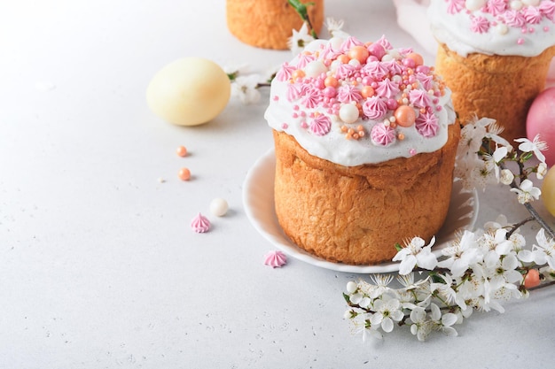 Traditional Easter sweet bread or cakes with white icing and sugar decor colored eggs and cherry blossom tree branch over white table Various Spring Easter cakes Happy Easter day Selective focus