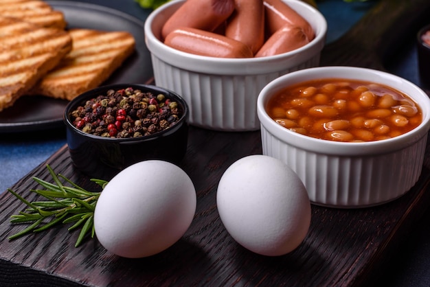 Traditional English breakfast with eggs toast sausages beans spices and herbs on a grey ceramic plate