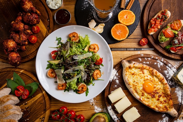 Foto cucina europea tradizionale, insalata con frutti di mare, khachapuri, bruschette, cosce di pollo. vista dall'alto.