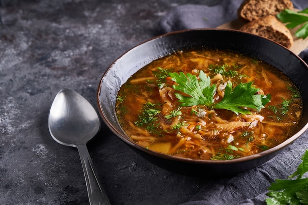 Traditional European and Russian soup borsch with cabbage and meat served in a plate on a dark stone table.