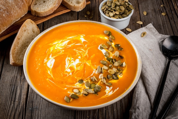 Piatti tradizionali autunnali e invernali, zuppa calda e speziata di zucca con semi di zucca, panna e baguette appena sfornate, sul vecchio tavolo di legno rustico,