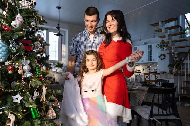a traditional family of mom dad and daughter near the christmas tree