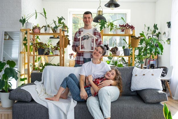 Foto una famiglia tradizionale con bambino si sta godendo la nuova casa seduta sul divano e con in mano il tetto assicurazione e protezione ipotecaria acquistando e trasferendosi nella propria casa verde con piante in vaso