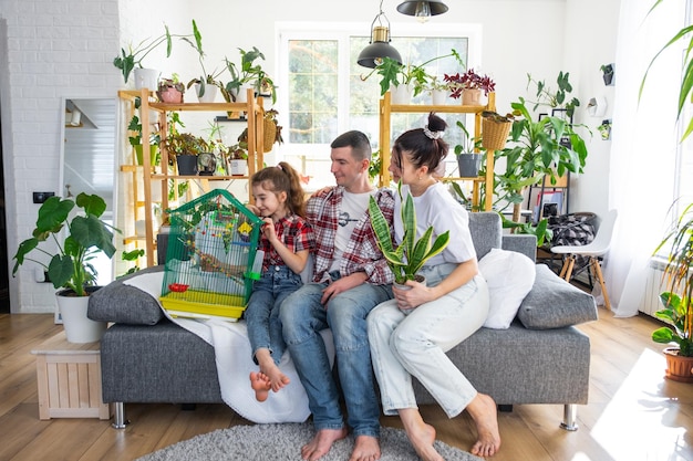 Foto una famiglia tradizionale con un bambino e un pappagallo in gabbia si gode una nuova casa seduta sul divano e tiene il tetto acquistando un'assicurazione ipotecaria e traslocando nella propria casa