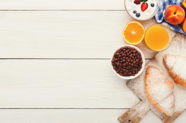 Traditional french breakfast menu background. Yogurt with fresh berries, glass of orange juice, muesli and croissants on wooden table, top view, copy space