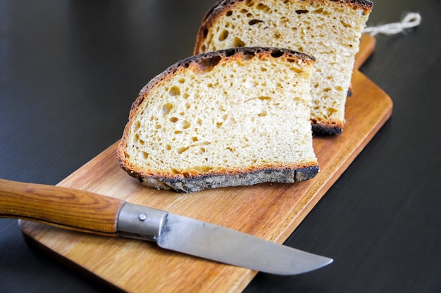 Fette di pane di campagna francese tradizionale e coltellino tascabile su un tagliere di legno.