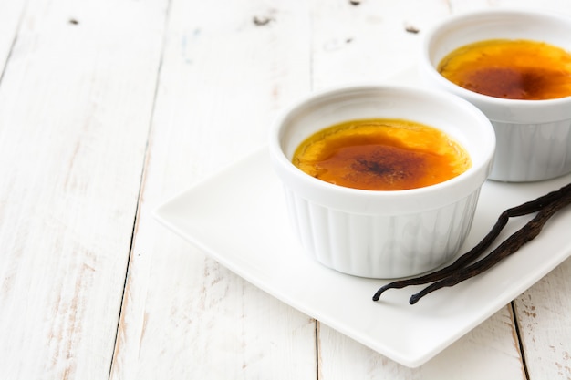 Traditional French creme brulee dessert with caramelized sugar on white wooden table copy space