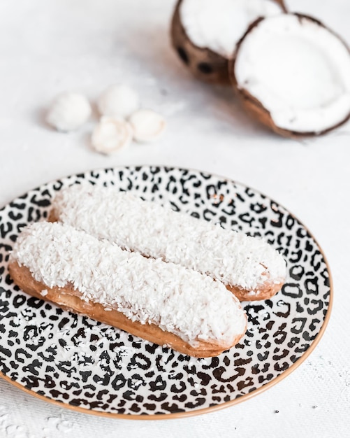 Traditional French dessert eclairs with coconuts in a composition on a white table and plate In the background coconut in half in a cafe or restaurant