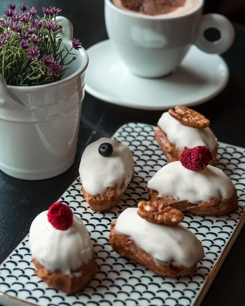 Traditional French dessert eclairs with white chocolate on black table in cafe or restaurant Hot chocolate drink and tea near by