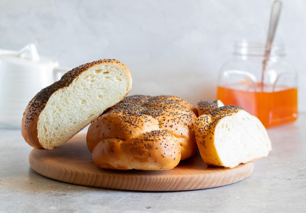 Traditional freshly baked Jewish pastries One and a half halas of homemade halas and slices on a wooden board a jar of apricot jam and a teapot Side view white background closeup