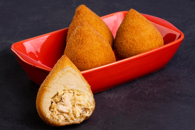 Traditional fried coxinha in a red container on a slate stone.