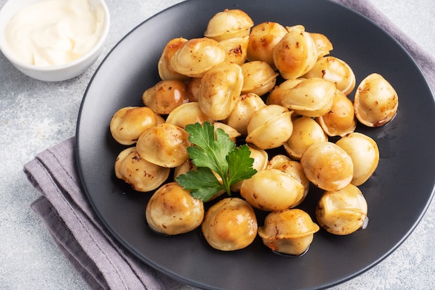 Traditional fried pelmeni, ravioli, dumplings filled with meat on black plate, russian kitchen. Gray concrete background, copy space.