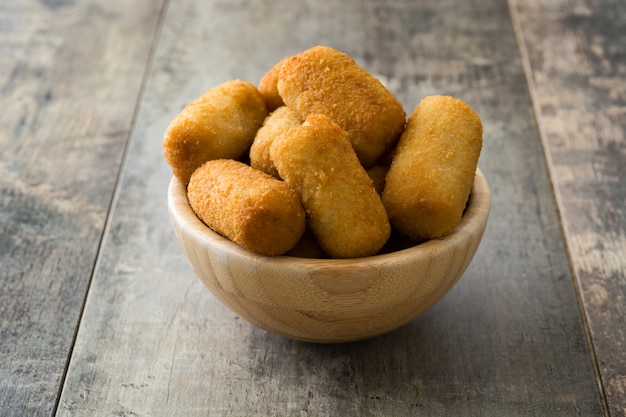 Traditional fried Spanish croquetas (croquettes) in bowl on wooden background