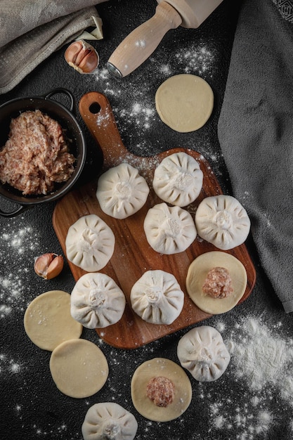 Traditional frozen homemade georgian khinkali or manty dumplings Ravioli set on a wooden cutting board on a dark table top view flat lay