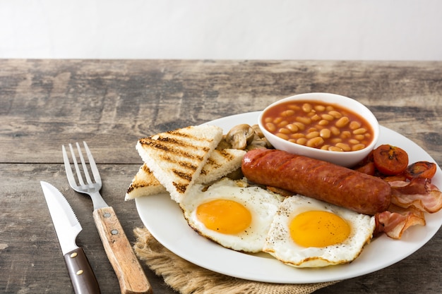 Traditional full English breakfast with fried eggs, sausages, beans, mushrooms, grilled tomatoes and bacon on wooden surface