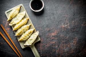 Traditional gedza dumplings on a cutting board with soy sauce.