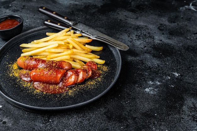 Traditional German currywurst, served with French fries. Black background. Top view. Copy space.