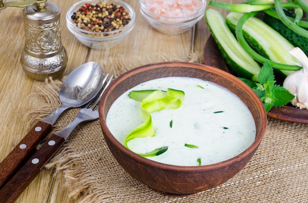 Traditional greek dip sauce or dressing tzatziki prepared with grated cucumber, yogurt, olive oil and fresh dill on wooden table in ceramic bowl.