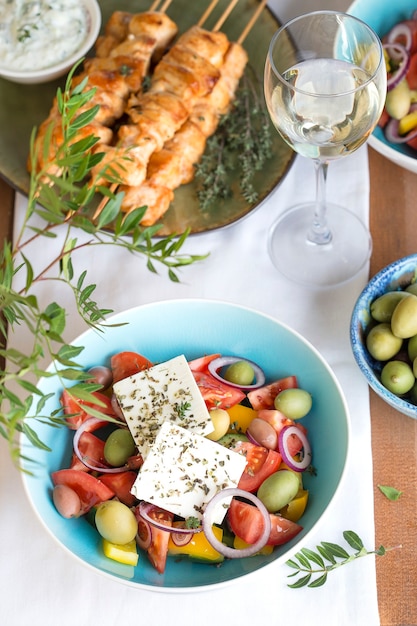 Традиционный греческий обед: салат с фетой, сувлаки, оливками и вином на большом столе.