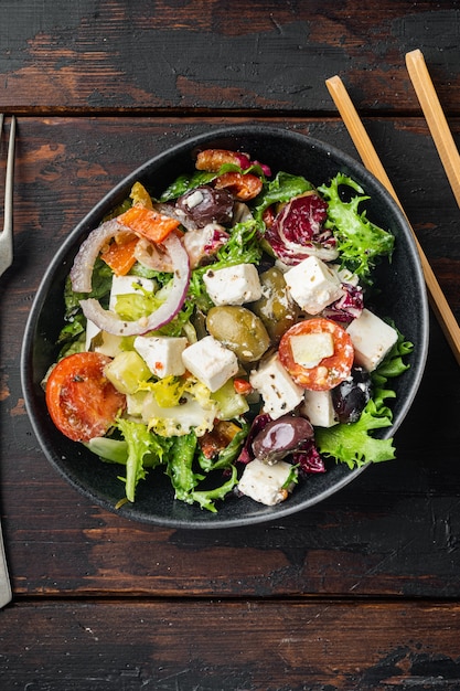 Traditional greek salad with fresh vegetables, feta and olives, on old dark  wooden table background, top view flat lay